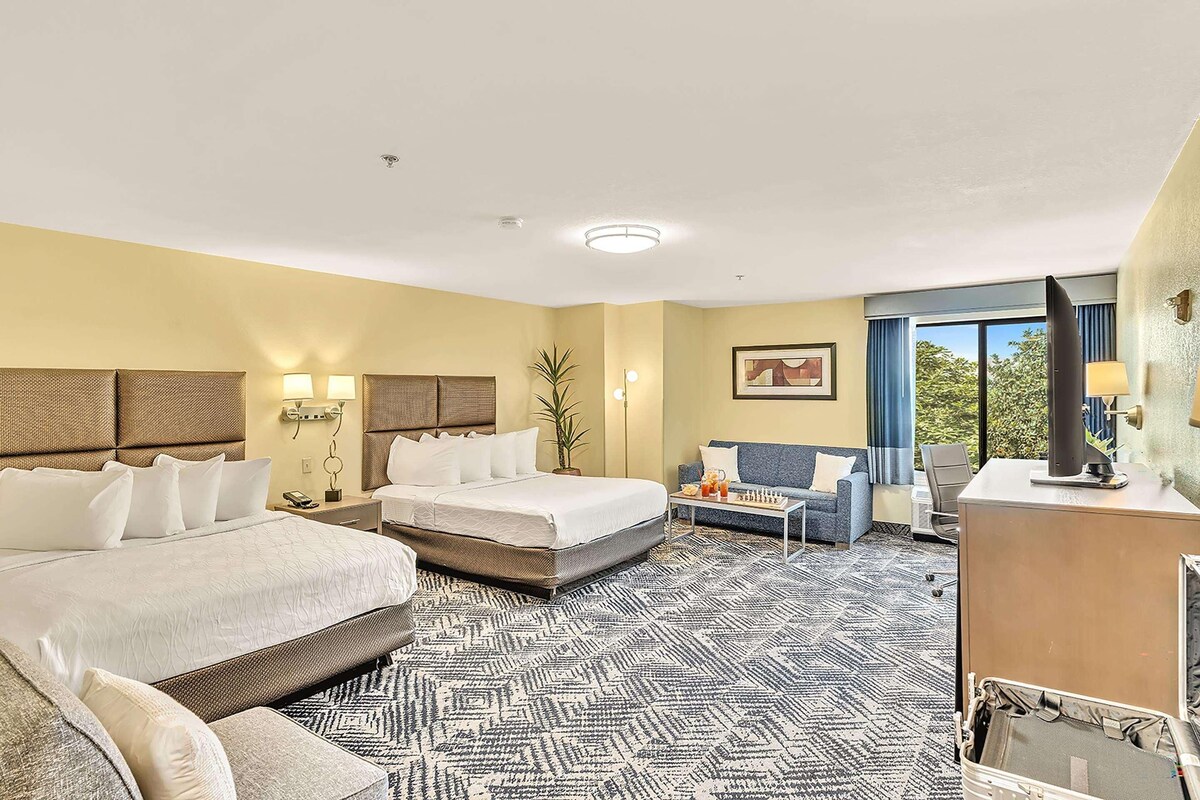 A hotel room with two beds, a sofa, a desk, and a large window.