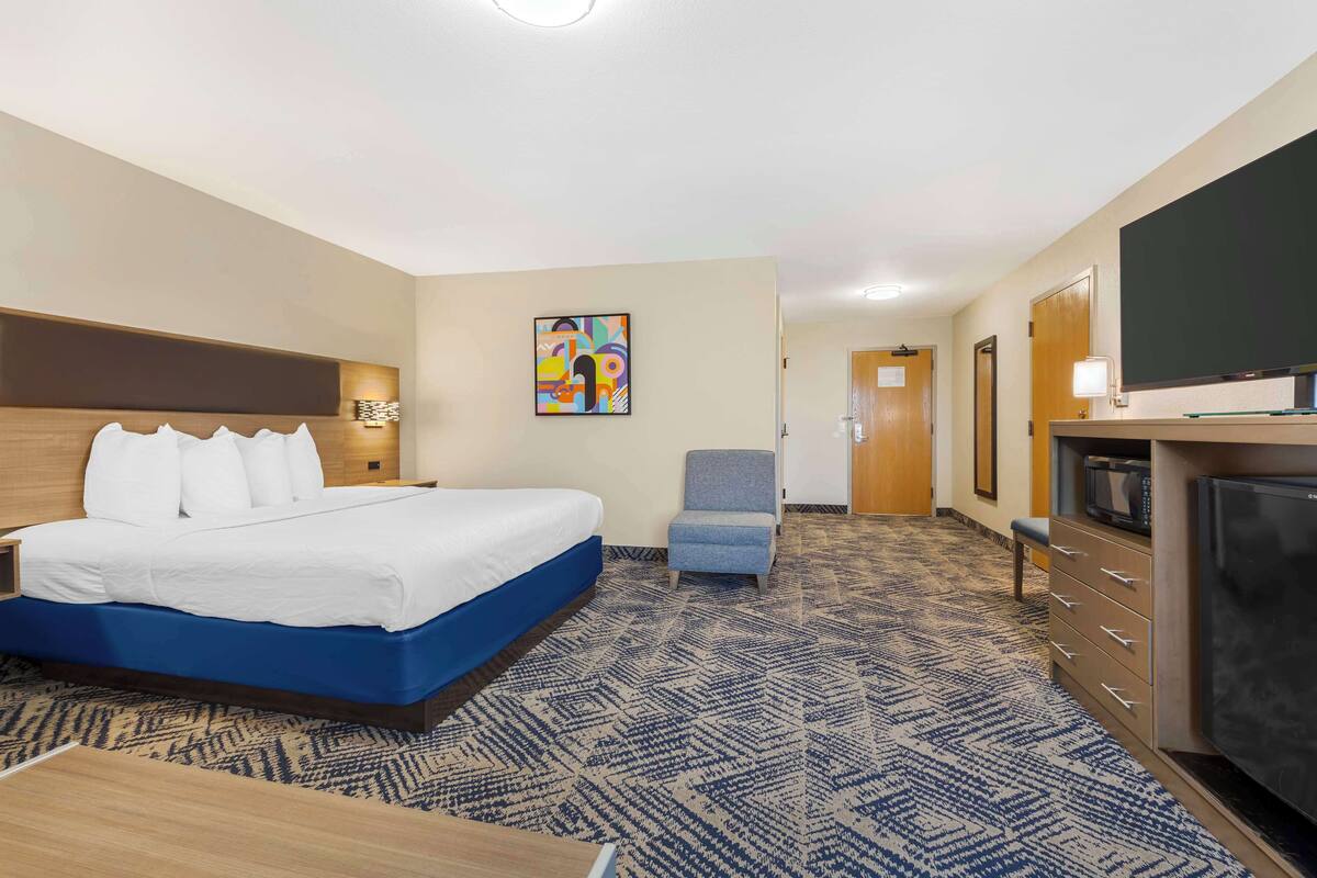 A hotel room with a bed, a chair, a TV, and a desk.