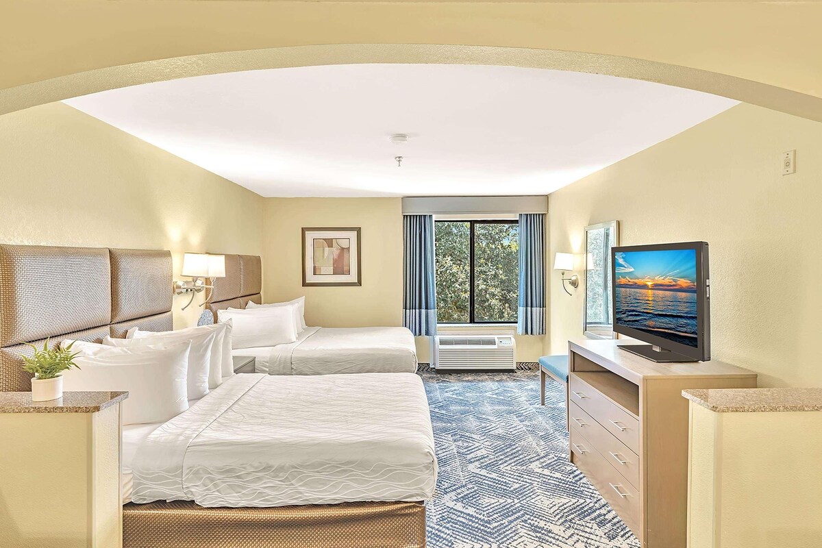 A hotel room with two beds, a TV, a desk, and a window with curtains.
