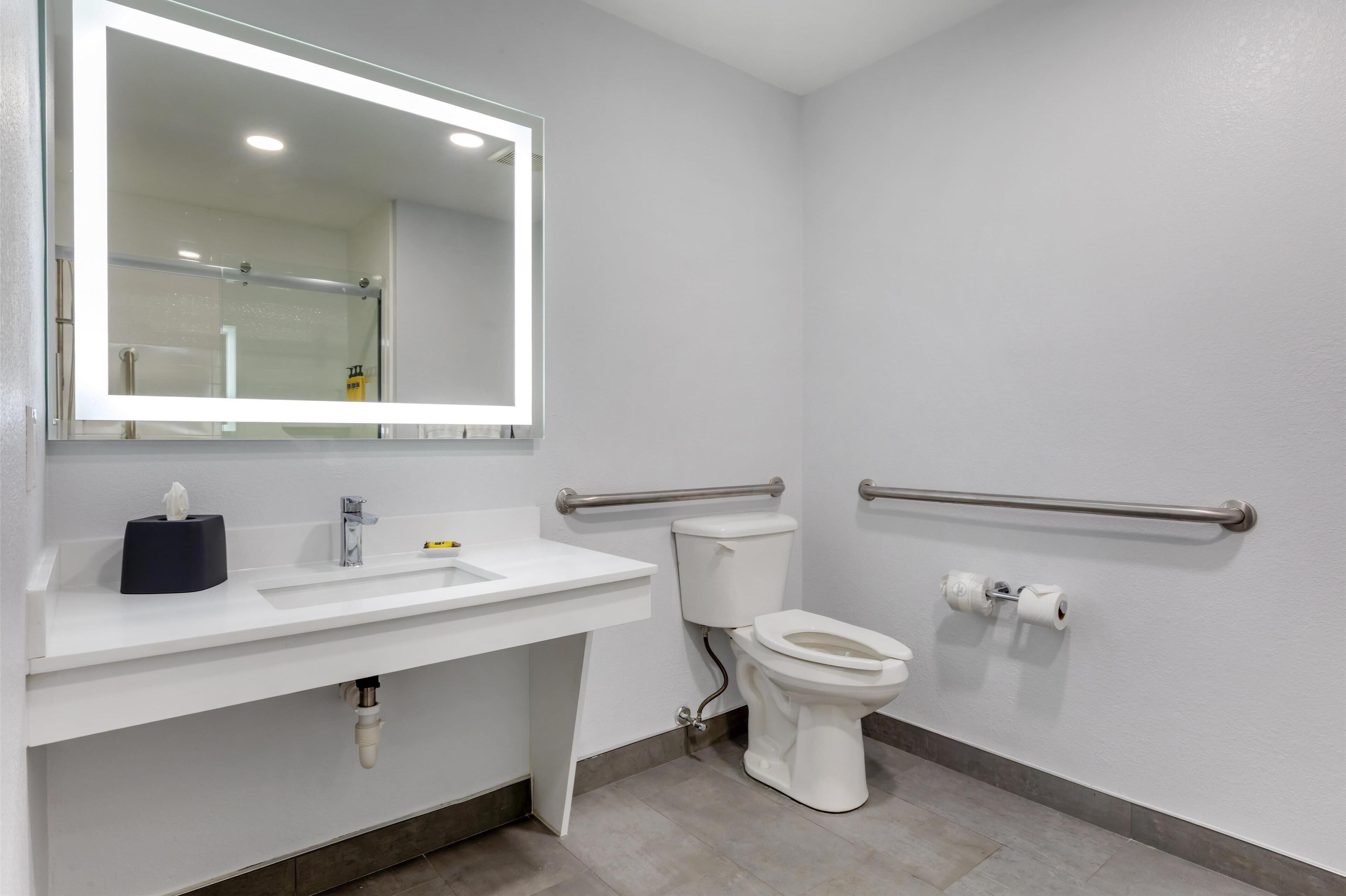 Une salle de bain moderne avec un lavabo blanc, des toilettes et un miroir doté d’un éclairage intégré.