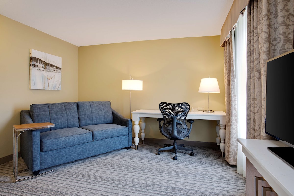 Habitación de hotel con un sofá azul, un escritorio con lámpara, una silla y un televisor.