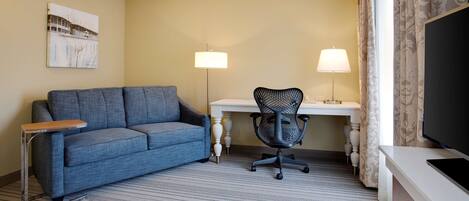 Une chambre d’hôtel avec un canapé bleu, un bureau avec une lampe, une chaise et un téléviseur.