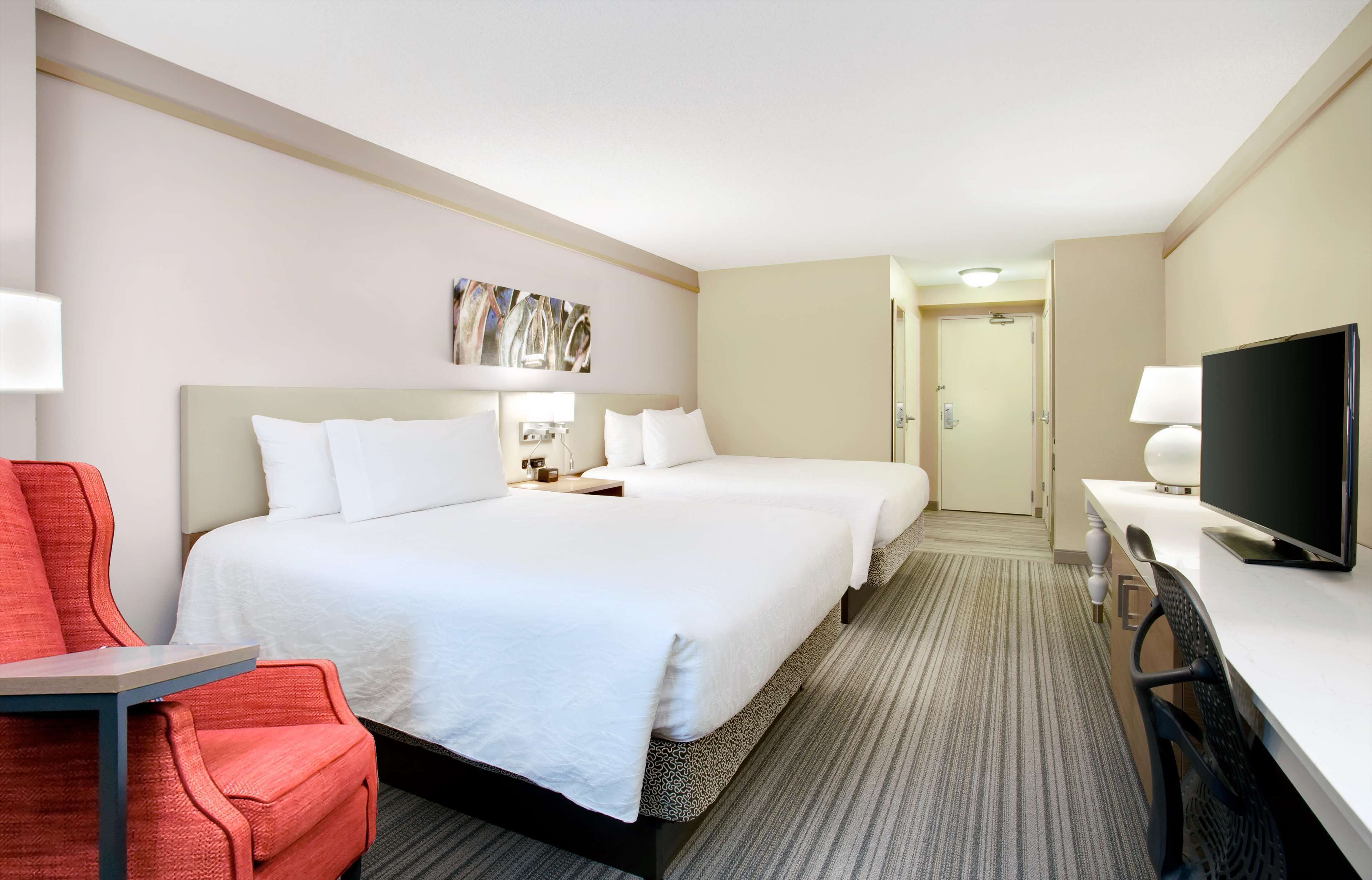 Une chambre d’hôtel avec deux lits, un bureau, une télévision et une chaise rouge.