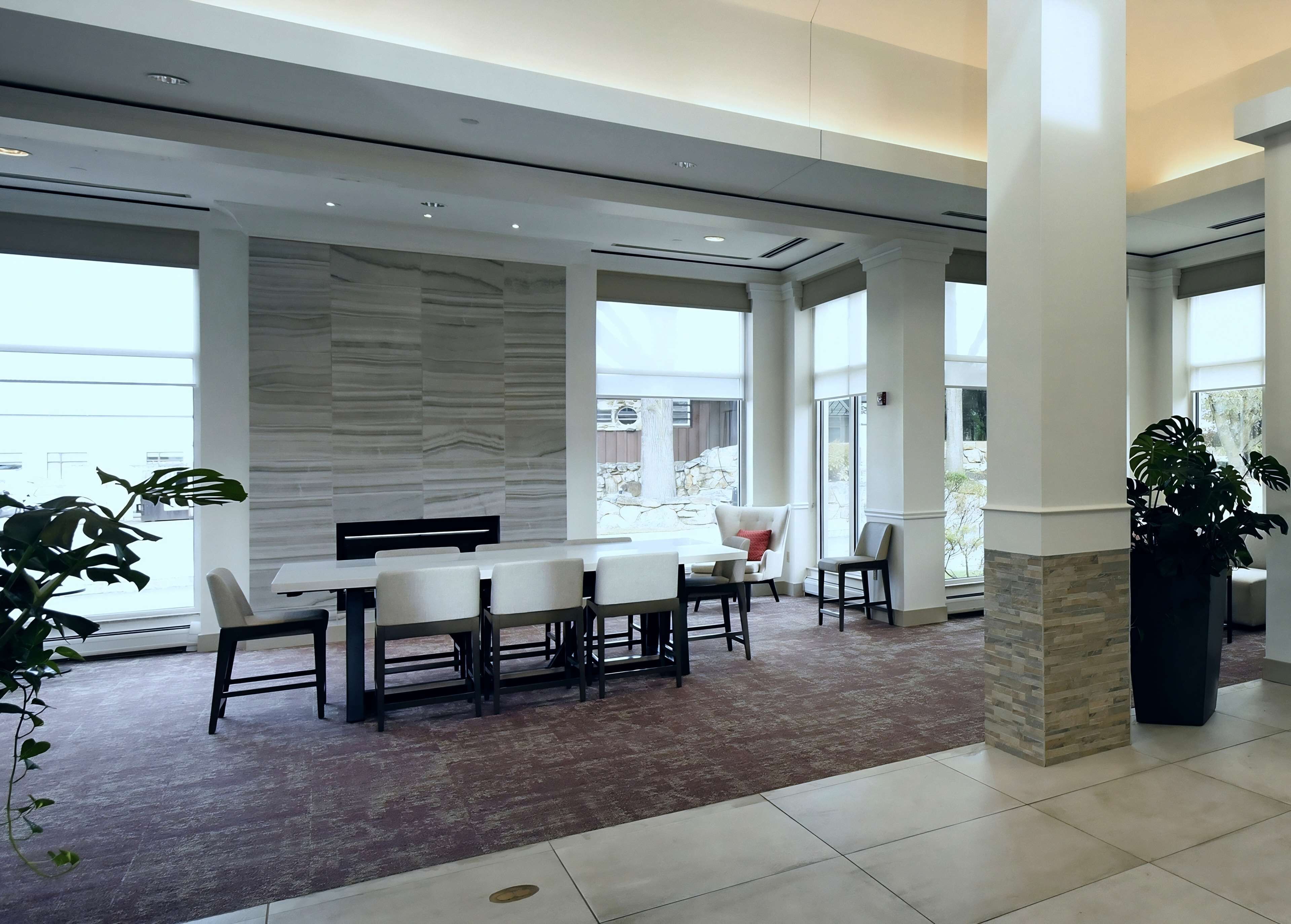 A spacious dining area with a long table and chairs, large windows, and a stone accent wall.