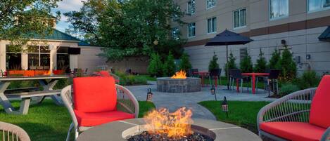 An outdoor patio area with a fire pit, red chairs, and a dining table.