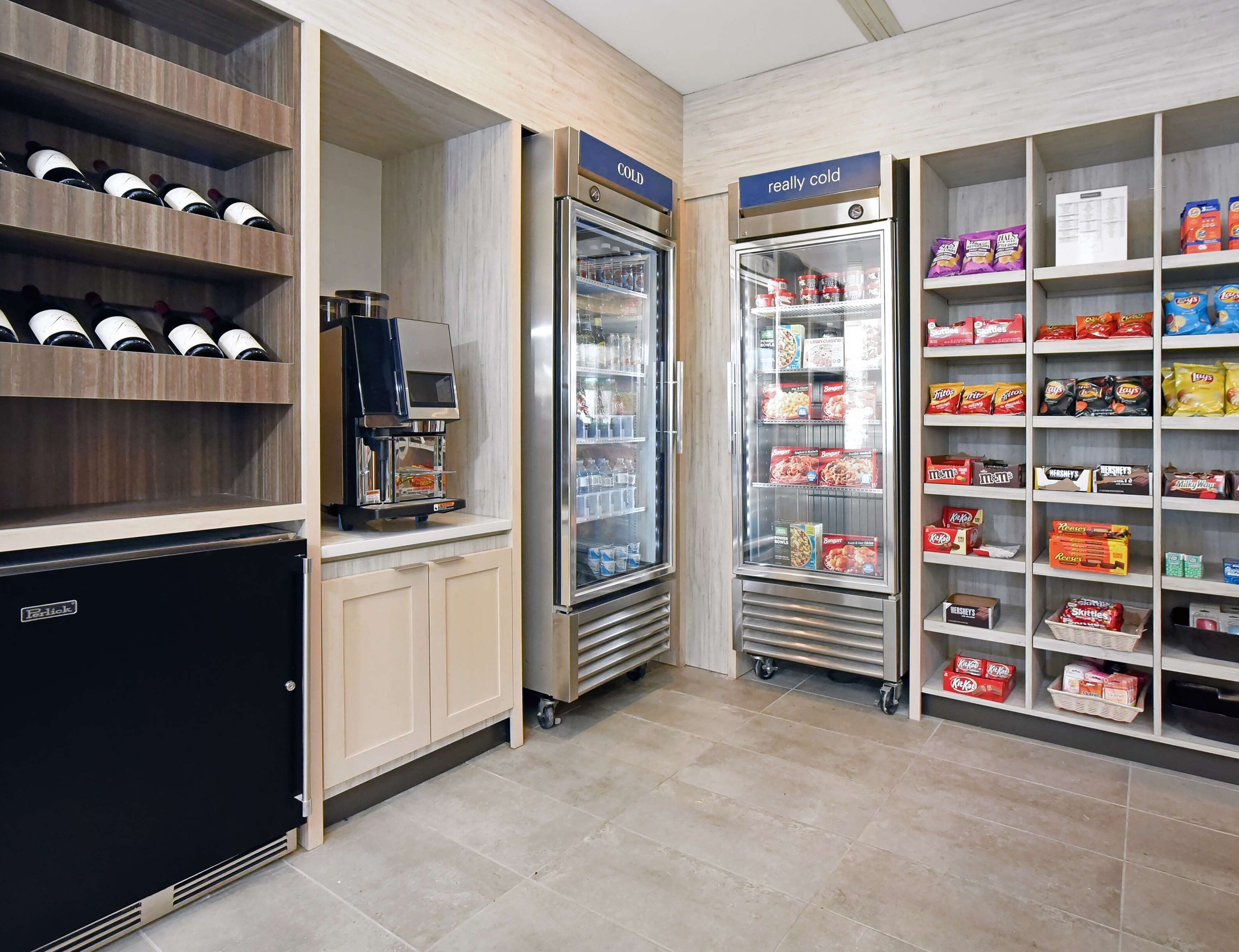 Een zelfbedieningsdrankenstation met een koffieapparaat, twee gekoelde vitrines en planken vol snacks en drankjes.