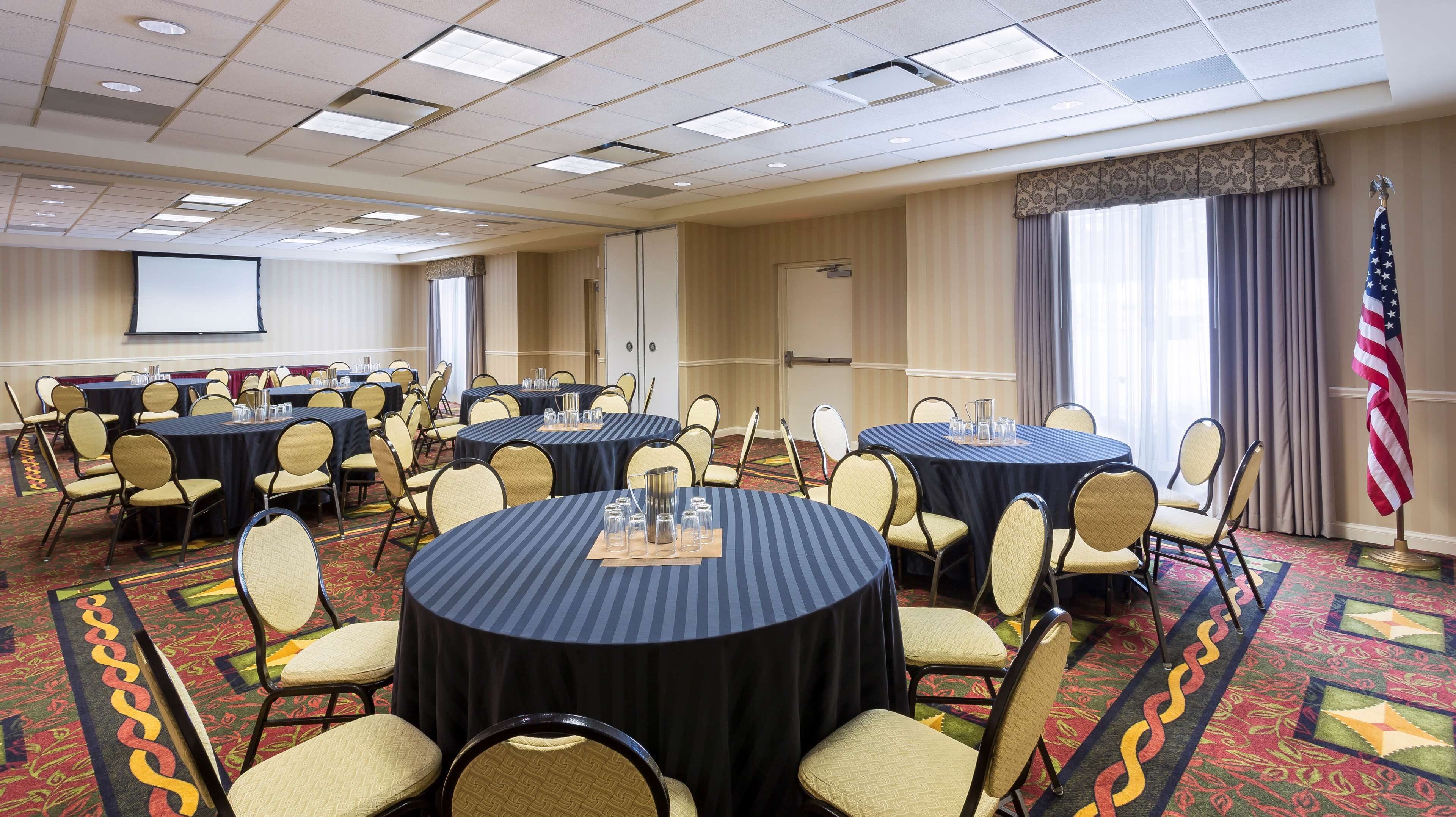 A conference room with multiple round tables, each with chairs and glassware.