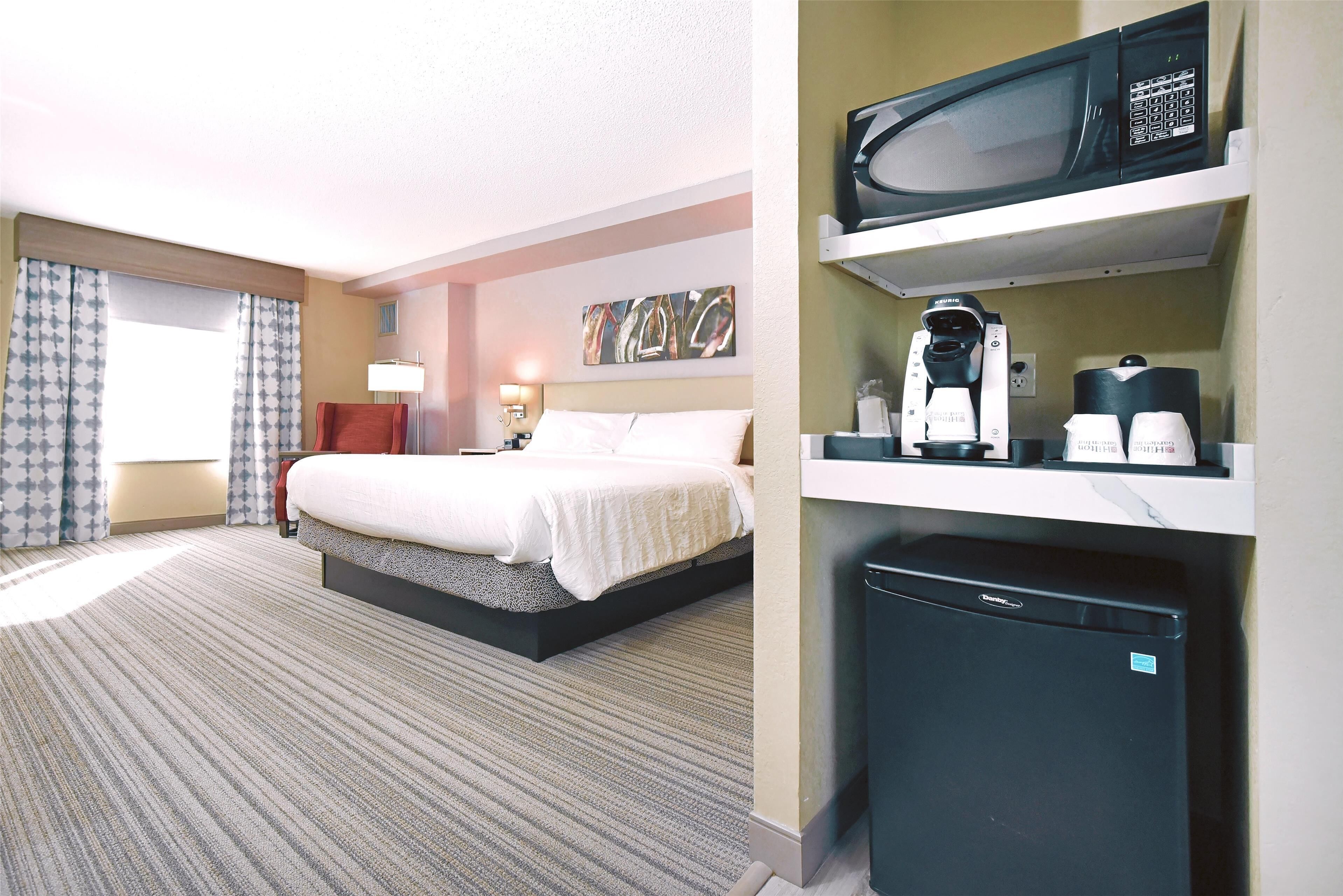 A hotel room with a bed, a desk, a microwave, and a coffee maker.