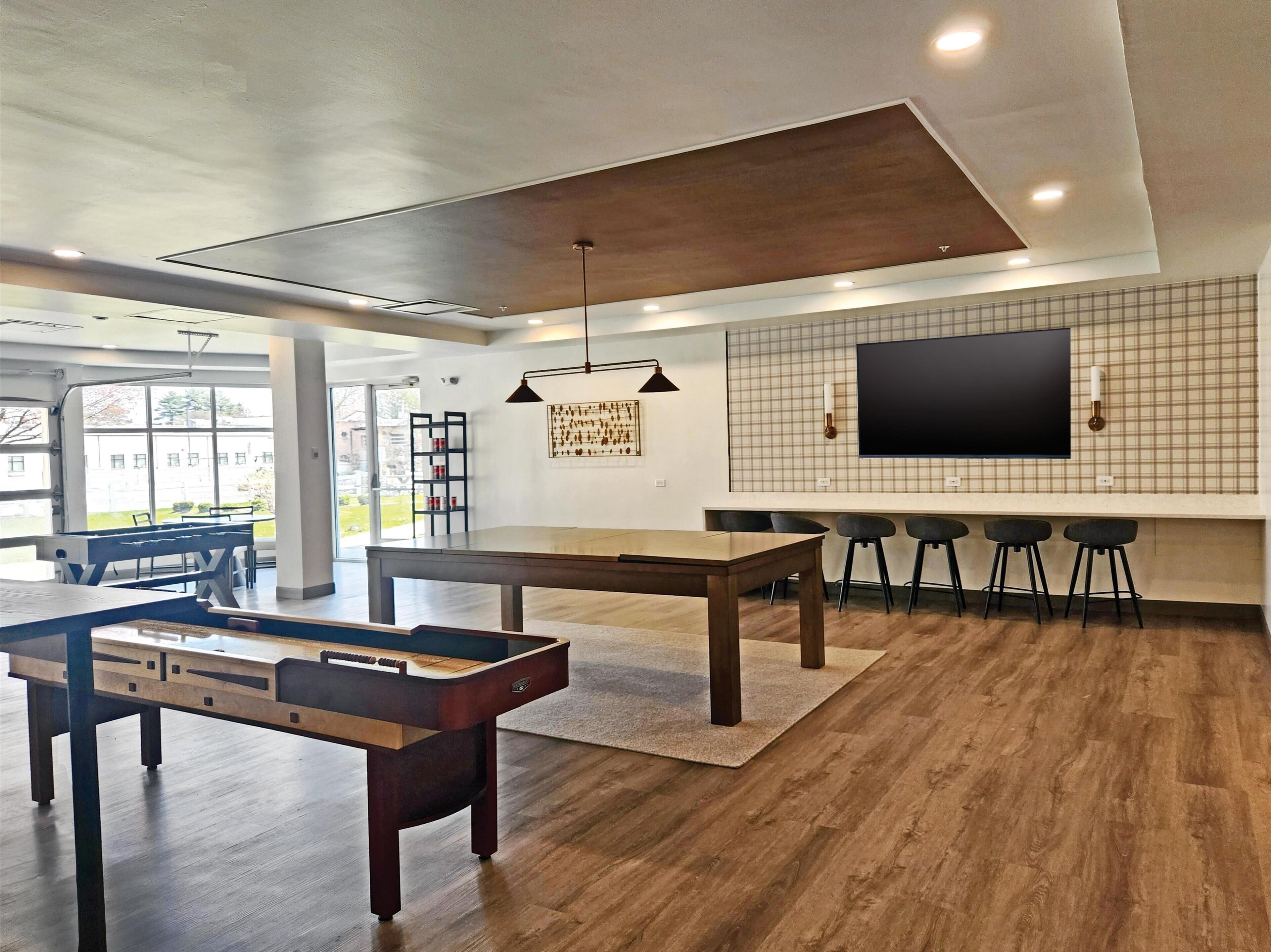 A modern living room with a foosball table, a large TV mounted on a grid-patterned wall, and a bar area with stools.