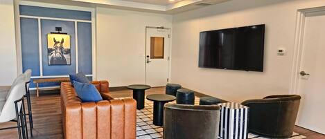 A modern living room with a leather sofa, round ottomans, and a flat-screen TV mounted on the wall.