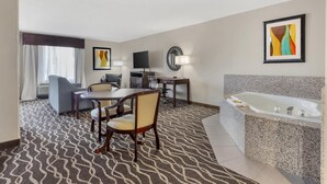 Habitación de hotel con comedor, televisor, escritorio, silla, sofá, espejo grande, lámpara y bañera.