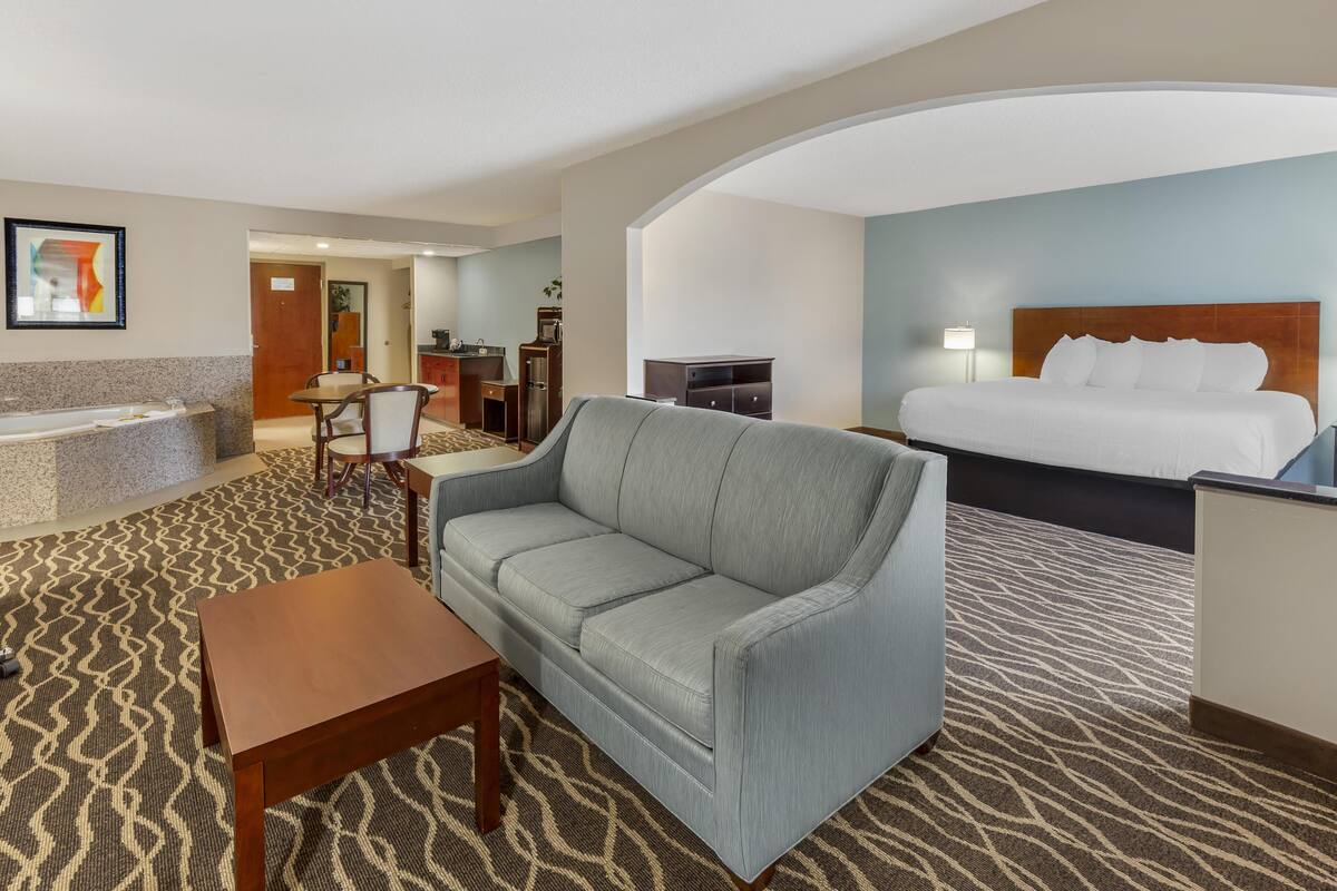 Une chambre d’hôtel comprenant un lit, un canapé, un bureau, une chaise, une table basse et une salle de bain avec baignoire.