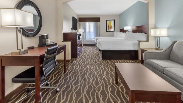 Habitación de hotel con escritorio, dos camas, sofá, televisor y cafetera.