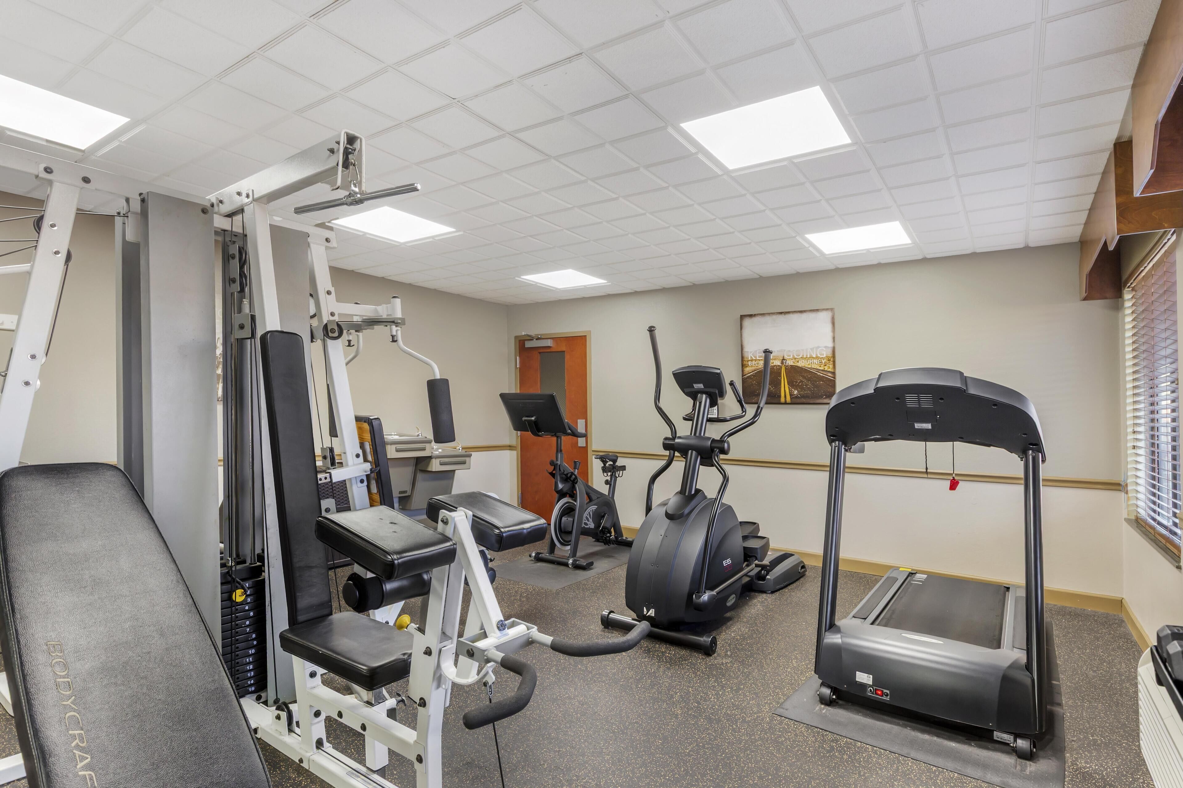 Une salle de sport équipée de divers appareils d’exercice, notamment un banc, des machines de musculation, un vélo elliptique et un tapis de course.