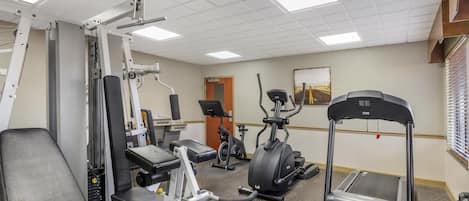 Een sportschool met diverse fitnessapparaten, waaronder een bank, gewichtmachines, een hometrainer en een loopband.