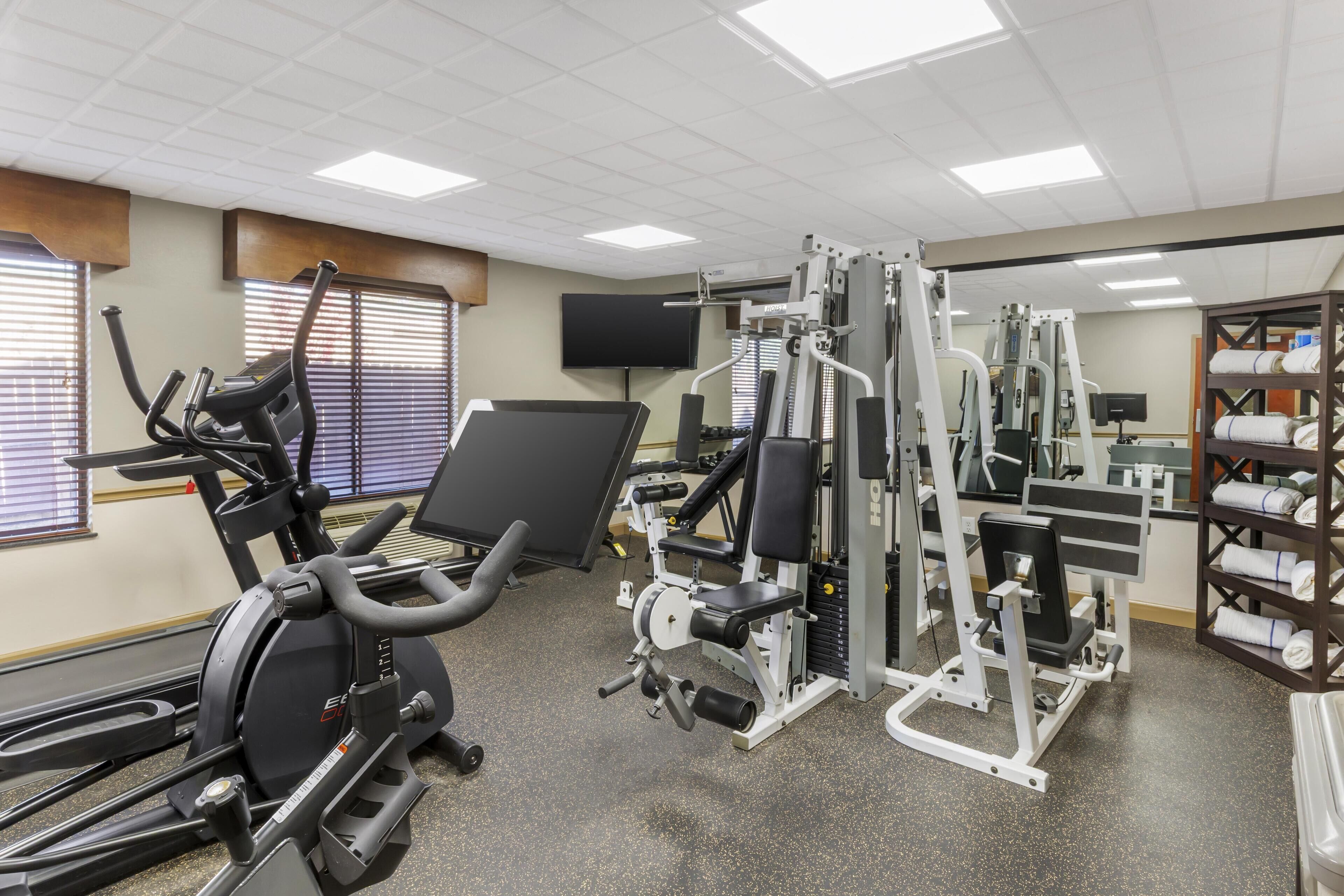 A gym with cardio machines, weightlifting equipment, and a television screen on the wall.