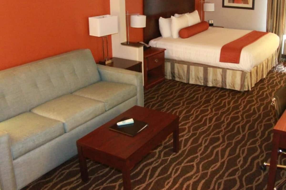 Une chambre d’hôtel avec un lit, un canapé, une petite table et un tapis à motifs.