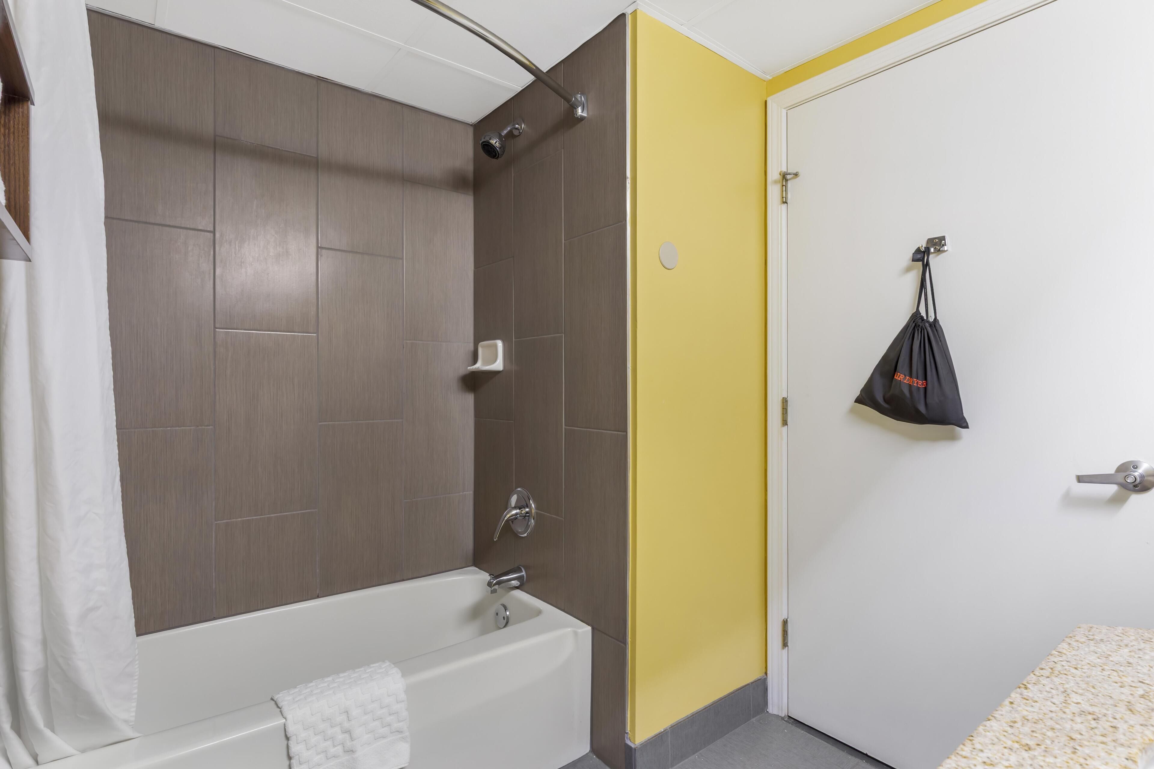 A bathroom with a bathtub, shower, and a yellow accent wall.