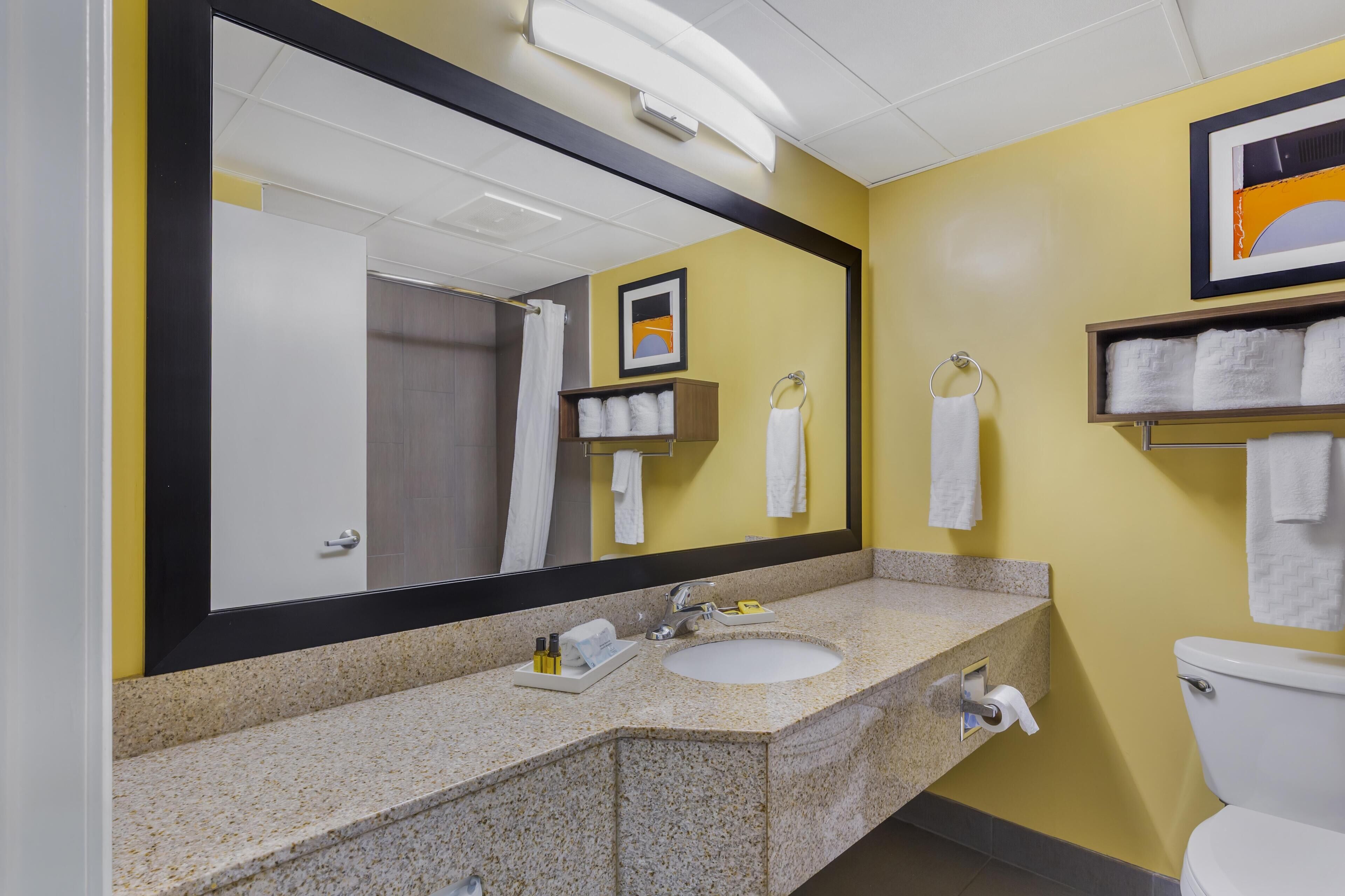 A bathroom with a sink, mirror, and toilet. There are towels on the wall and a framed picture above the mirror.