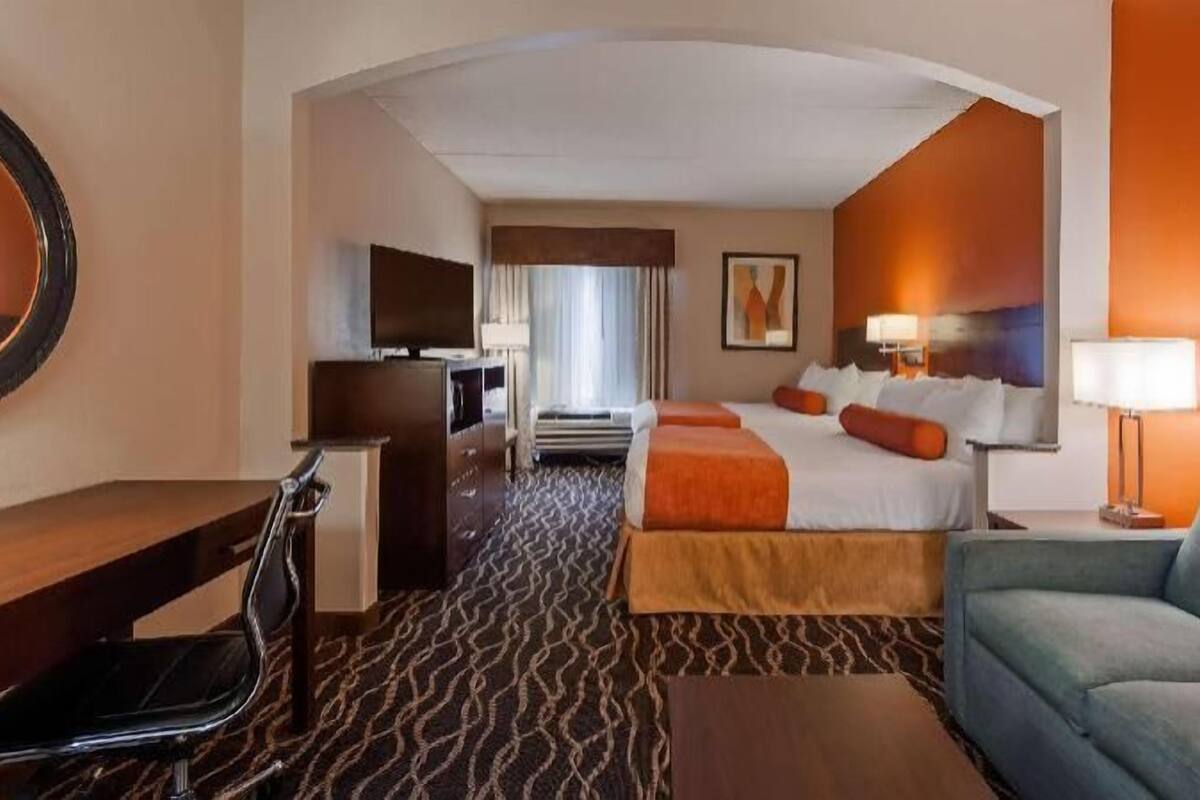 Une chambre d’hôtel équipée d’un lit, d’un bureau, d’une chaise, d’un canapé, d’une télévision et d’un miroir fixé au mur.