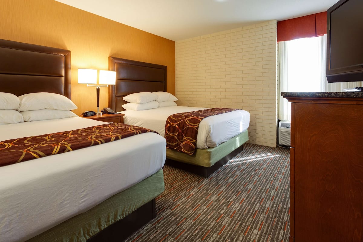 A hotel room with two beds, a TV, a nightstand, and a brick wall.