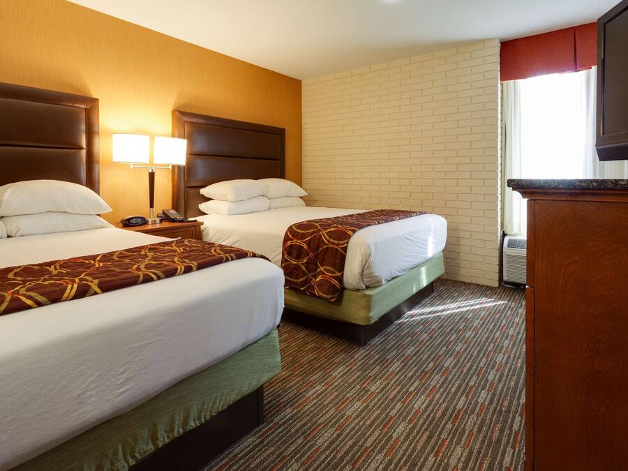A hotel room with two beds, a TV, a nightstand, and a brick wall.