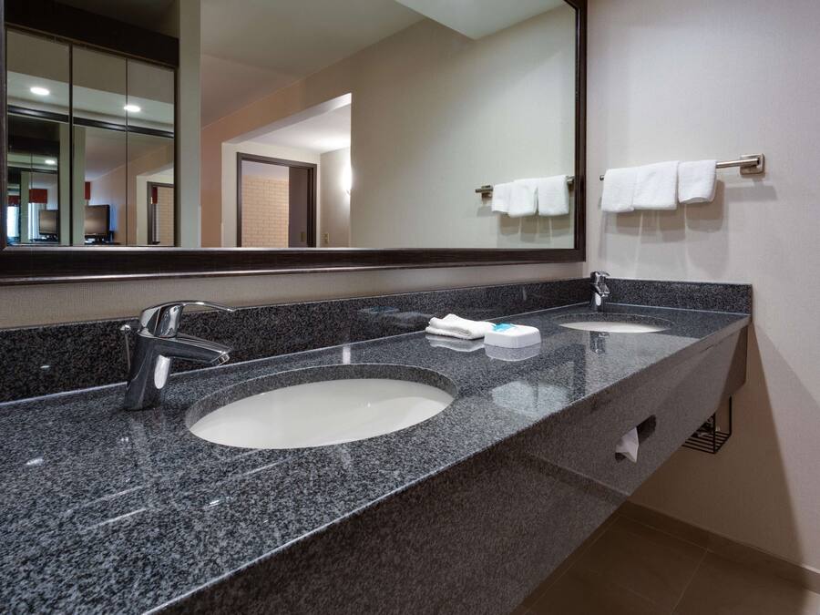 Un baño moderno con encimera de granito, dos lavabos, un espejo grande y un perchero para toallas.