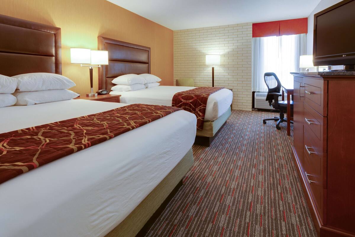 A hotel room with two beds, a desk, a chair, a TV, and a dresser.