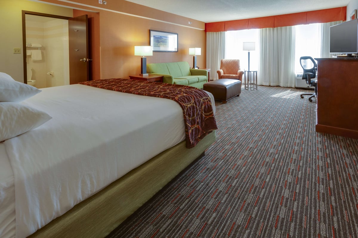 A hotel room with a large bed, a green sofa, a desk with a chair, and a television.