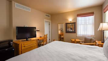 A hotel room with a bed, a desk with a computer, a TV, a chair, a lamp, and a window with curtains.
