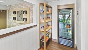 A reception area with a reception desk, a wall-mounted clock, a wooden shelf with snacks, and a beverage refrigerator.