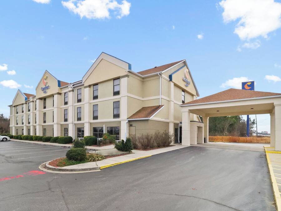 A hotel with a covered entrance, a parking lot, and a clear sky.