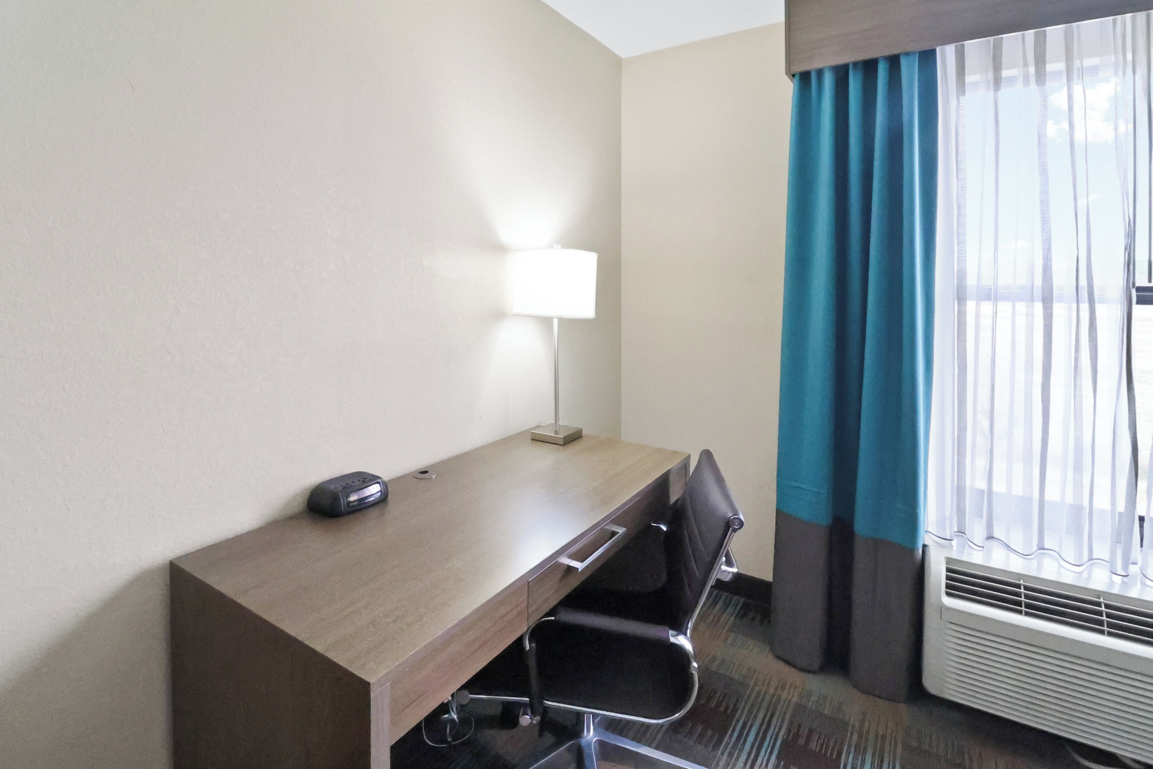 Een hotelkamer met een houten bureau, een stoel, een lamp en een raam met gordijnen.