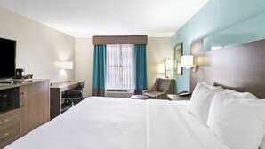 A hotel room with a large bed, a desk with a computer, a chair, a TV, and a window with curtains.