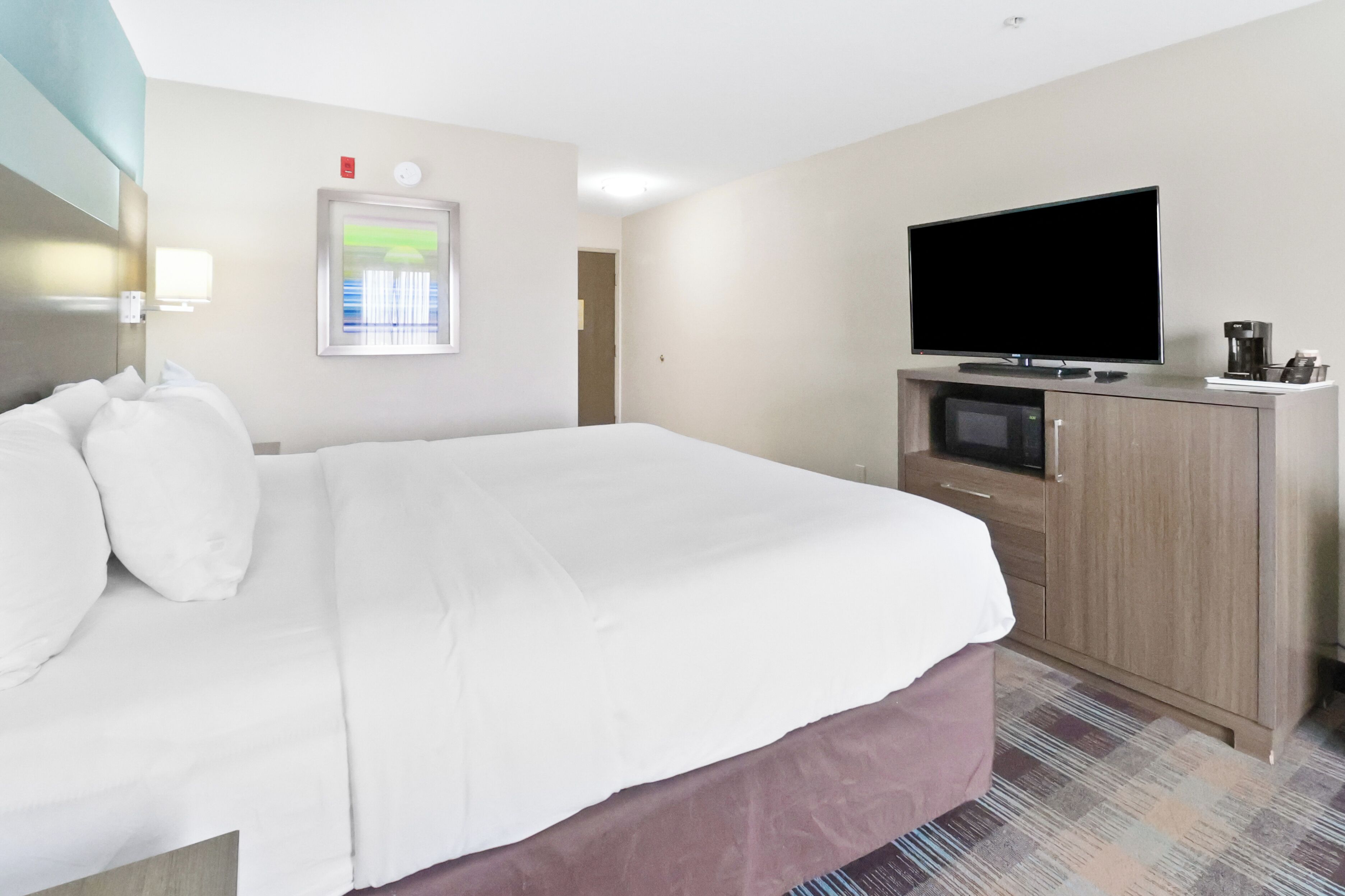 Une chambre d’hôtel dotée d’un grand lit, d’une télévision à écran plat, d’un four à micro-ondes et d’une machine à café.