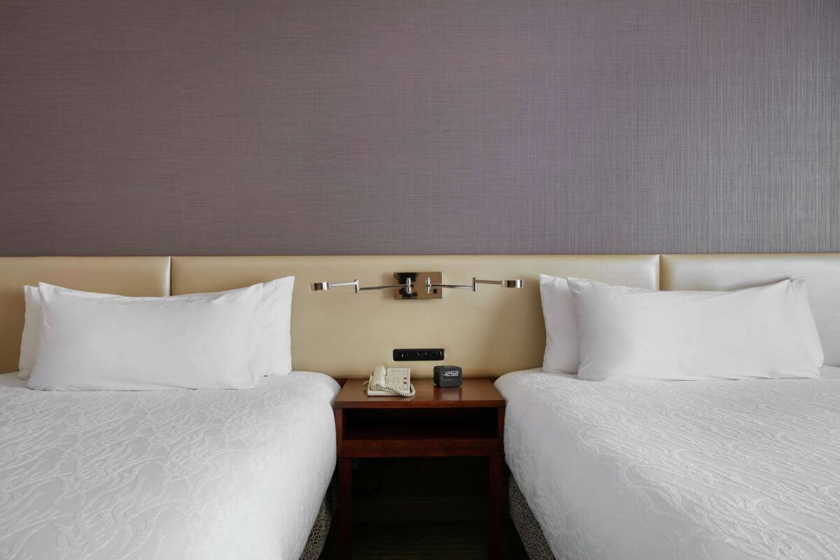 Ein Hotelzimmer mit zwei Betten, einem Nachttisch mit Telefon und Uhr sowie einer strukturierten Wand.