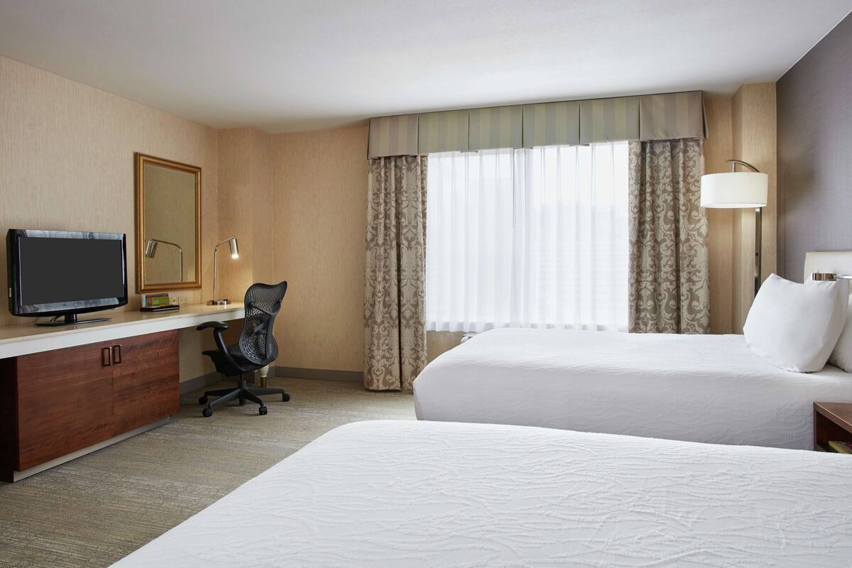 Ein Hotelzimmer mit Bett, Schreibtisch mit Computer, Stuhl, Fernseher und Vorhängen.