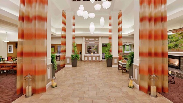 Een hotel lobby met een centraal receptiegedeelte, grote zuilen en hangende pendelverlichting.