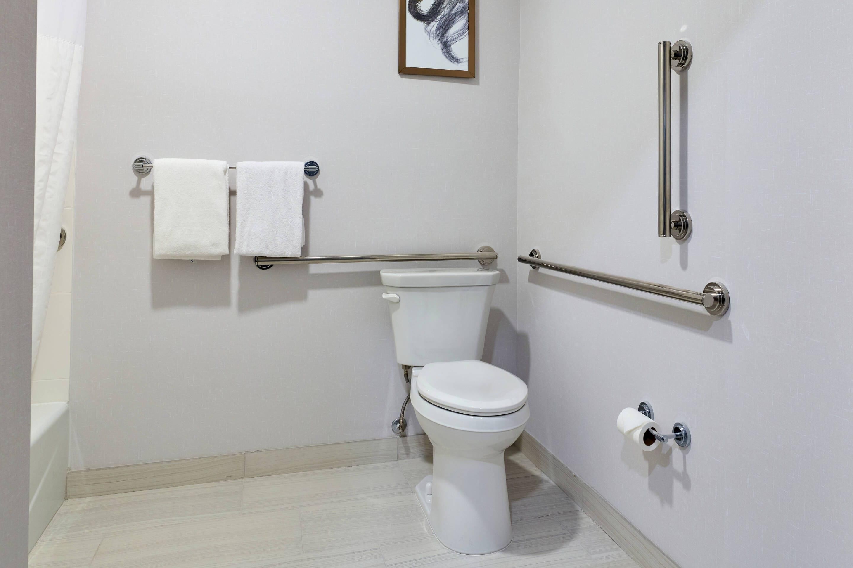 A bathroom with a toilet, two towels, a handrail, and a toilet paper holder.