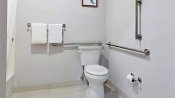 A bathroom with a toilet, two towels, a handrail, and a toilet paper holder.