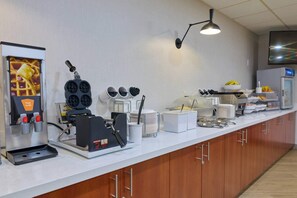 A modern kitchen area with a coffee machine, waffle maker, and various kitchen utensils.