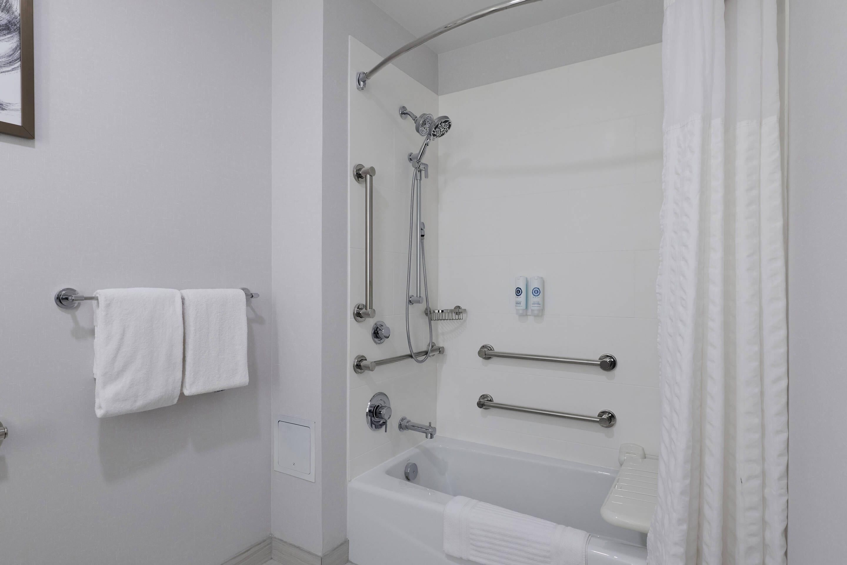 A bathroom with a bathtub, shower, and handrails.