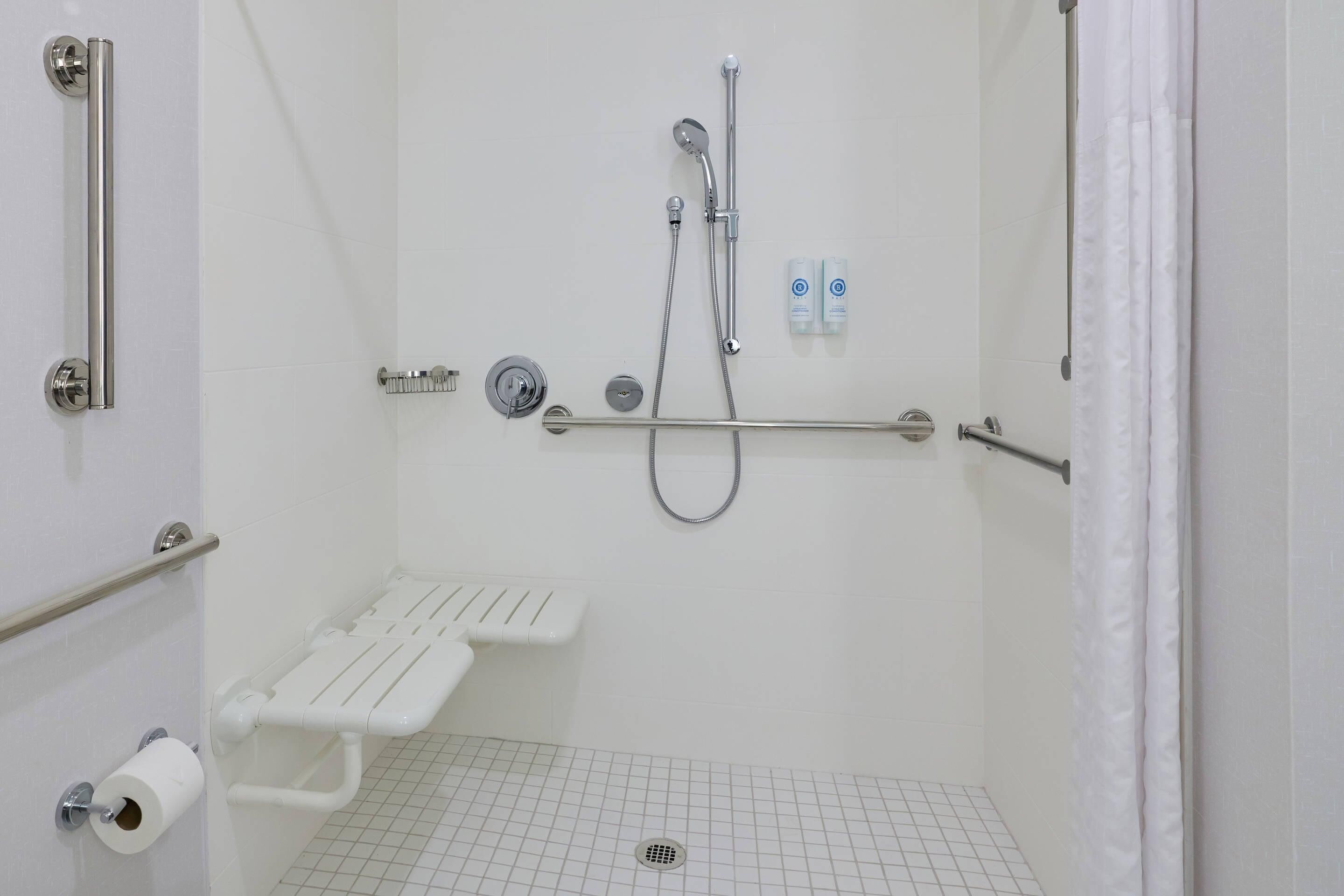 A bathroom with a shower, grab bars, a toilet paper holder, and a handrail.