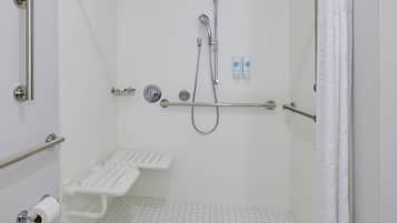 A bathroom with a shower, grab bars, a toilet paper holder, and a handrail.