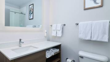 Ein modernes Badezimmer mit Waschbecken, Ablagefläche und Toilette in Weiß. Handtücher hängen an der Wand, über dem Spiegel befindet sich ein gerahmtes Bild.