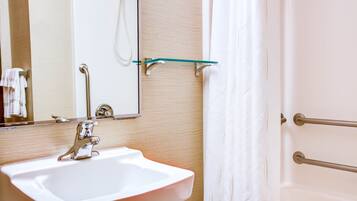A bathroom with a white sink, a mirror, a glass shelf, and a shower curtain.