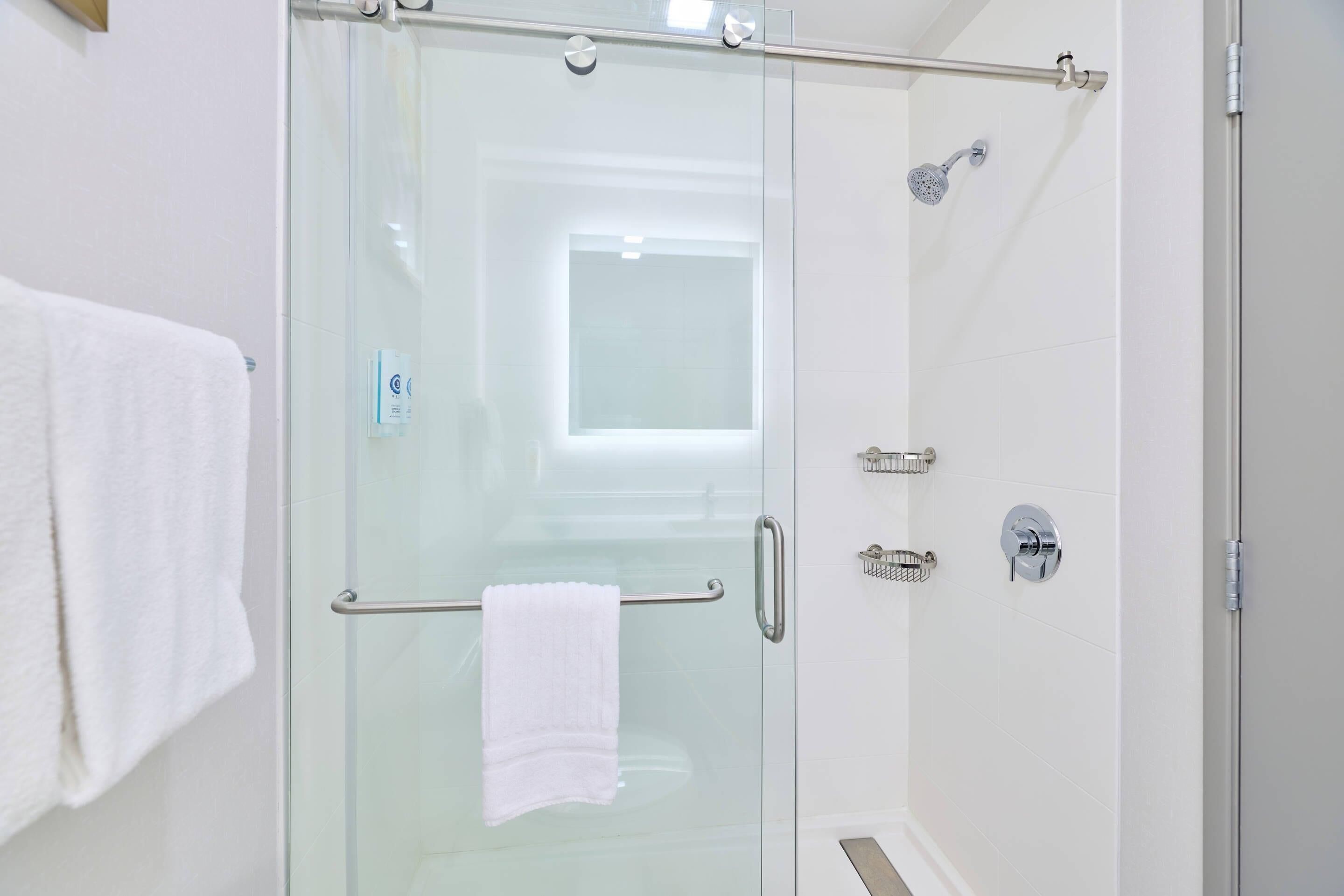 A glass-enclosed shower with a towel rack, a handheld showerhead, and a wall-mounted faucet.