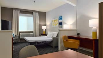Una habitación de hotel con cama, escritorio, silla, televisión y ventana con cortinas.