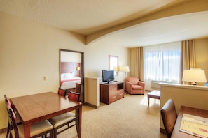 A hotel room with a wooden desk, a television, a sofa, a chair, and a bed with a red headboard. - Comfort Suites Springfield-Eugene (Springfield)