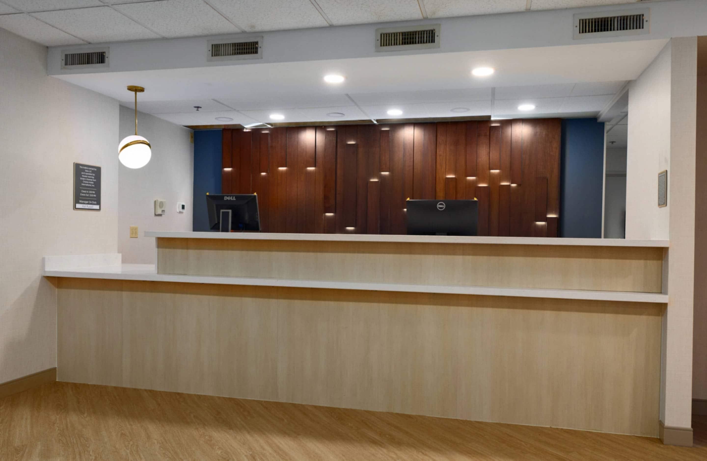 A reception desk with two computers, wooden paneling, and a light fixture.